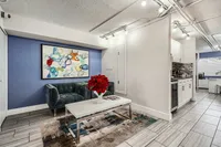 Chic apartment interior showcasing a modern lounge with a plush green sofa, vibrant abstract art, and sleek kitchen design.