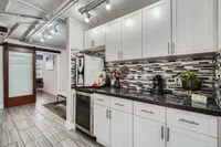 Chic modern kitchen featuring sleek white cabinets, elegant backsplash, and cozy coffee nook under stylish track lighting.