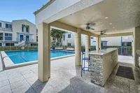 Inviting outdoor area featuring a sparkling pool, covered bar with high stools, and modern apartment backdrop.