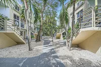 Modern apartment complex with tropical landscaping, featuring palm trees and a serene pathway leading to charming entrances.