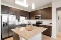 Modern kitchen featuring sleek dark wood cabinets, granite countertops, and stainless steel appliances, opening into a stylish dining area for luxurious living.