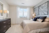 Inviting bedroom with elegant decor, featuring modern art, plush pillows, and ample natural light through large windows.