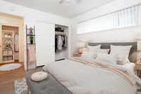 A Modern bedroom with bed and accent pillows with a pink hue throw blanket. There are clothes in the closet showing storage pace. The light from the window above the bed creates a warm atmosphere.