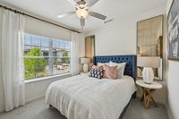 Bright bedroom with a plush, navy-blue tufted headboard, elegant white bedding, and stylish decor. Sunlit by large windows with a serene outdoor view.