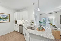 Bright and modern kitchen featuring sleek white cabinetry, stylish countertops, and pendant lighting, leading to a cozy living area with natural light and view.