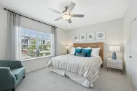 Bright and airy bedroom with elegant decor, featuring a plush bed with striped bedding, stylish lamps, and a comfortable teal armchair by a large window.