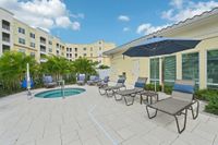 Inviting apartment complex courtyard featuring a cozy hot tub, stylish sun loungers, and lush greenery against a bright and welcoming building facade.