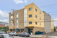 Modern yellow apartment building with street-facing windows and ground-floor businesses, offering contemporary urban living.