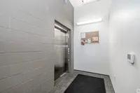 Modern apartment elevator lobby with sleek brushed metal doors, illuminated by bright overhead lighting, featuring a convenient bulletin board for community updates.