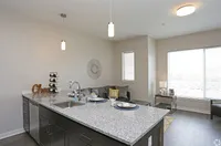 Modern apartment with open-concept kitchen and living room, featuring a sleek granite countertop, stylish pendant lighting, and bright natural light from large windows.