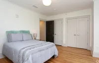 Inviting bedroom with sleek hardwood floors, soft grey bedding, and natural light, ideal for relaxation.