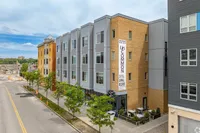 Modern urban apartment building with sleek architecture, featuring a blend of brick and metal facades, lined with trees on a bustling city street.