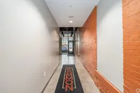 Chic industrial-style hallway with exposed brick and modern finishes, showcasing a welcoming entrance mat and sleek lighting.