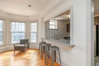 Bright and inviting living space featuring large windows, elegant hardwood floors, and a sleek breakfast bar with modern stools, perfect for entertaining.