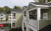 Charming two-story apartments with green siding and inviting balconies, nestled in a serene residential neighborhood.