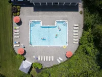 Aerial view of a luxurious outdoor pool with sun loungers, vibrant umbrellas, and lush greenery, perfect for relaxation and leisure.