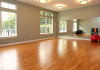 Spacious fitness studio with large windows, hardwood flooring, and mirrored wall, perfect for yoga or workouts.