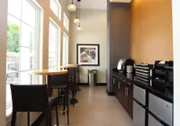 Modern coffee bar with sleek high-top tables, abundant natural light from tall windows, and stylish pendant lighting.
