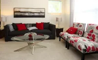 Inviting living room with a modern black sofa, vibrant red accents, chic floral armchairs, and a sleek glass coffee table.
