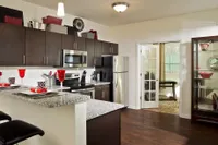 Modern kitchen with dark cabinetry, sleek appliances, and granite countertops, adjacent to a cozy dining area with elegant glassware and warm lighting.