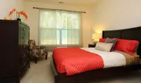 Inviting bedroom with a plush bed, vibrant orange accents, and a cozy chair, perfect for relaxation and comfort.