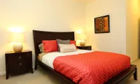 Cozy bedroom featuring a luxurious bed with vibrant orange bedding and elegant wooden furniture, illuminated by warm bedside lamps.