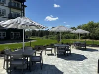 Charming outdoor dining area with sleek patio furniture and elegant striped umbrellas, surrounded by lush greenery and a serene landscape.