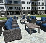 Spacious and stylish apartment patio featuring elegant wicker seating with plush blue cushions, surrounded by a well-maintained outdoor area.