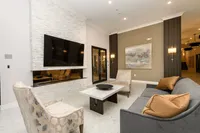 Elegant living room with a sleek modern fireplace, large wall-mounted TV, and plush seating. Stylish decor includes a marble coffee table and sophisticated lighting fixtures.