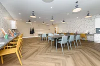 Modern community room featuring stylish wooden flooring, ample seating with colorful chairs, and elegant pendant lighting, perfect for gatherings and creative activities.