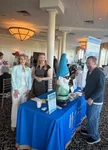 Vibrant networking event with smiling attendees and a whimsical gnome statue at a blue-branded display table.
