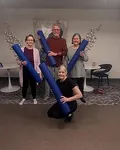 Spacious and inviting community room with four joyful individuals holding yoga mats, highlighting a vibrant and friendly living environment.