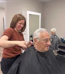 Friendly hair stylist giving a professional haircut to a smiling elderly man in a welcoming salon.