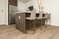 Modern kitchen area with sleek stainless steel appliances, stylish island with elegant bar stools, and inviting wood flooring.