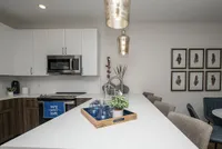 Modern kitchen with sleek white cabinets, stainless steel appliances, and elegant pendant lighting over a spacious island. Includes chic decor and cozy seating area.