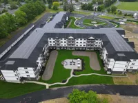 Aerial view of a modern, expansive apartment complex with a beautiful courtyard featuring green lawns and elegant seating areas.