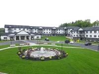 Charming apartment complex with lush green lawns, a decorative fountain centerpiece, and ample parking space, offering a welcoming community vibe.