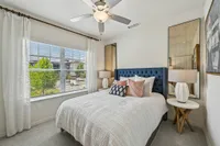 Bright bedroom with a plush, navy-blue tufted headboard, elegant white bedding, and stylish decor. Sunlit by large windows with a serene outdoor view.