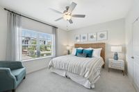 Bright and airy bedroom with elegant decor, featuring a plush bed with striped bedding, stylish lamps, and a comfortable teal armchair by a large window.