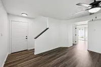 Inviting entryway with elegant dark wood flooring, fresh white walls, and a modern ceiling fan, leading to an open and airy living space with natural light.