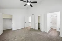 Modern bedroom with plush carpet flooring, elegant ceiling fan, spacious closets, and an adjacent bathroom entrance.