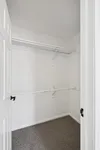 Spacious walk-in closet with ample shelving and hanging space, featuring clean white walls and plush carpeting.