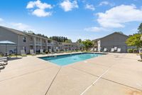 Inviting outdoor apartment pool area with lounge chairs and umbrellas under a bright blue sky, perfect for relaxation and enjoyment.