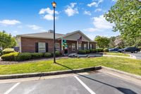 Charming red brick building with lush landscaping, colorful balloons, and an inviting entrance, perfect for a welcoming community vibe.