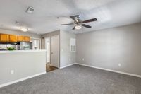 Inviting living space with textured carpet, modern ceiling fan, and an open kitchen featuring warm wooden cabinets and sleek countertops.