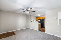 Modern open-concept living space with a cozy carpeted area, elegant ceiling fan, and functional kitchen featuring warm wooden cabinets.