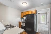 Charming kitchen in bright apartment featuring sleek black appliances, wooden cabinetry, and a cozy open layout leading to a sunlit living area.