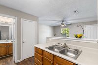 Inviting kitchen with sleek countertops, double sink, and warm wooden cabinetry, leading to a bright, open living space with a modern ceiling fan.
