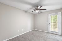 Bright room with plush carpeting, modern ceiling fan, and door leading to outdoor space, ideal for relaxation.