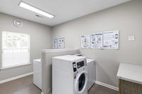 Bright and airy laundry room with modern washing machines, ample light from a large window, and helpful instructional posters.